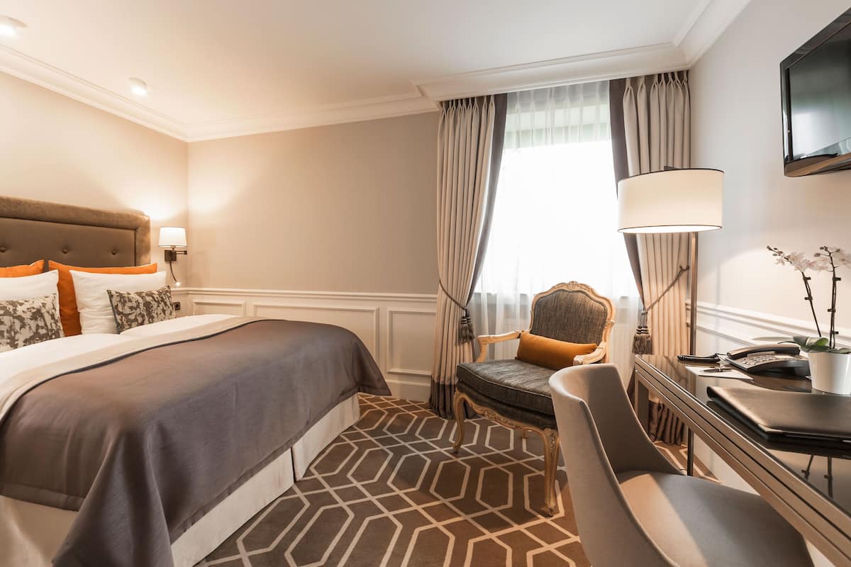 Een hotelkamer met een groot bed, een bureau met lamp, een stoel en een televisie die aan de muur is bevestigd.