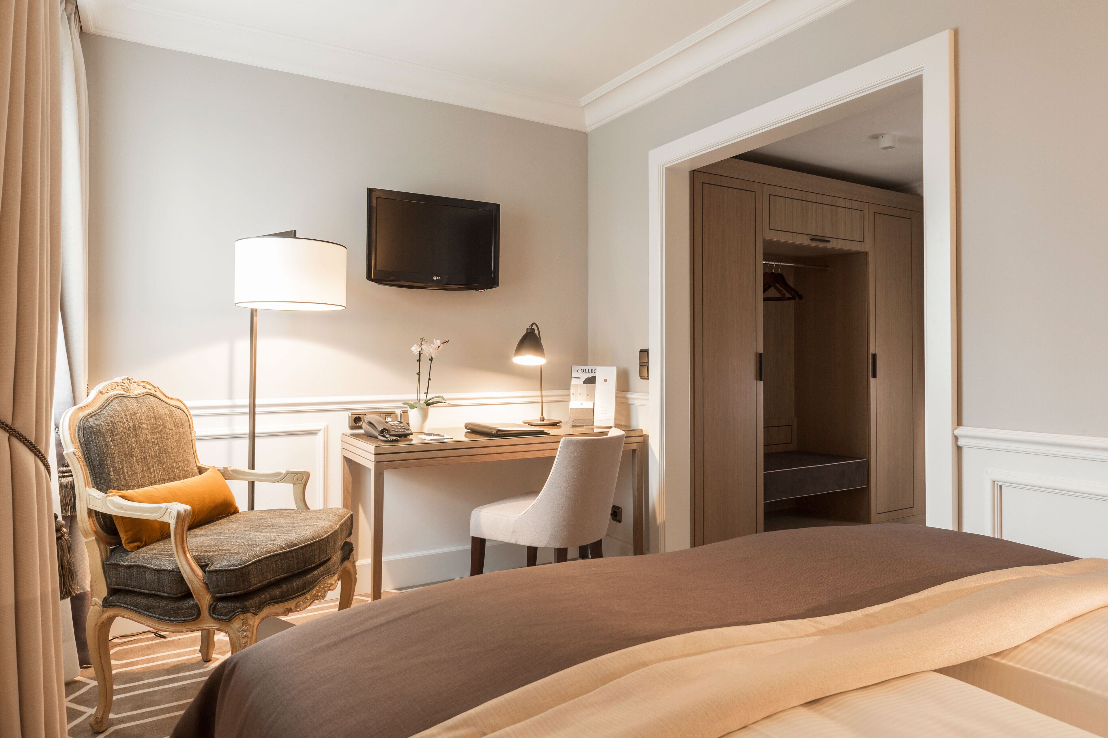 Habitación de hotel con cama, escritorio con lámpara, silla, televisión y vestidor.