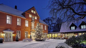 Un grand bâtiment à deux étages, dont le toit est recouvert de neige, et devant lequel se dresse un grand sapin de Noël.