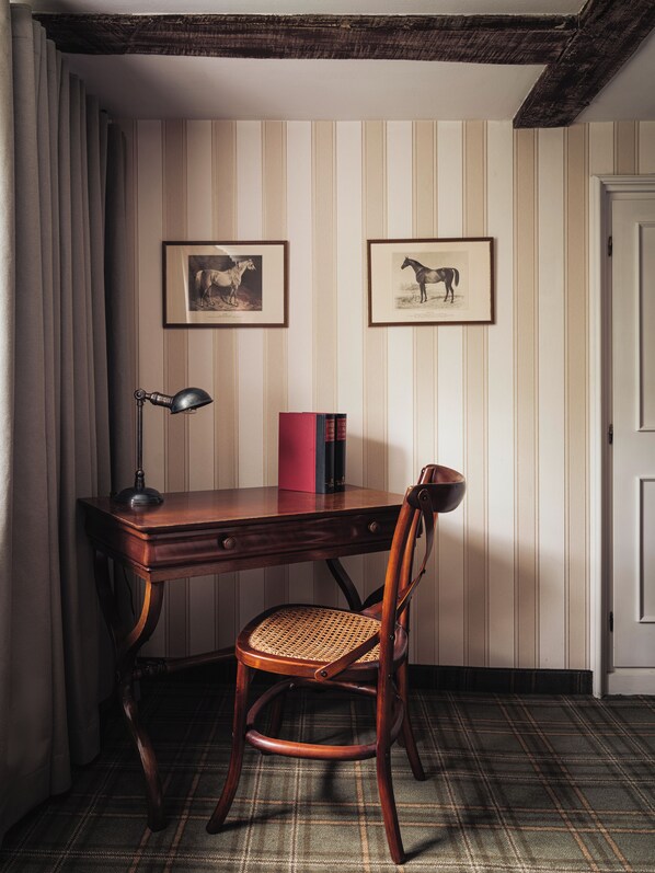 A study room with a wooden desk, a chair, a lamp, and two framed equine photographs on the wall.