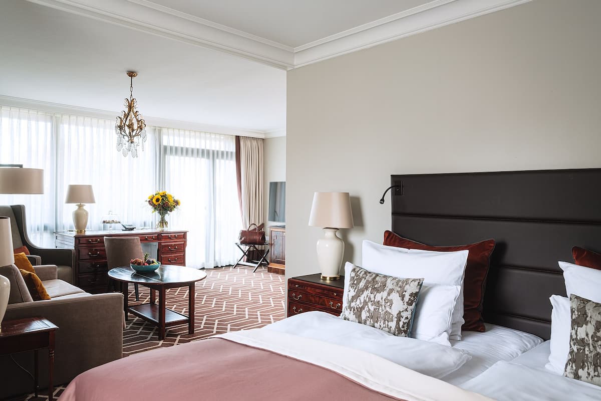 Hotelkamer met een groot bed, een bureau, een stoel, een lamp en uitzicht op het groen.