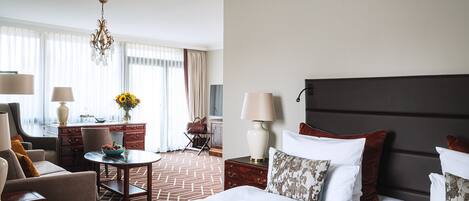 A hotel room with a large bed, a desk, a chair, a lamp, and a view of the outdoors.