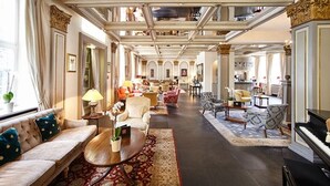 Un hall d’hôtel spacieux, agrémenté d’un magnifique escalier, de fauteuils confortables et d’un piano.