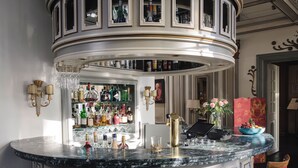 Un espace bar doté d’un comptoir en marbre, de nombreuses bouteilles d’alcool, de verres et d’une caisse enregistreuse.