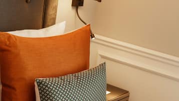 A neatly made bed with white sheets, a brown headboard, and two pillows, one orange and one patterned green.
