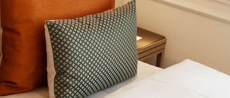 A neatly made bed with white sheets, a brown headboard, and two pillows, one orange and one patterned green.