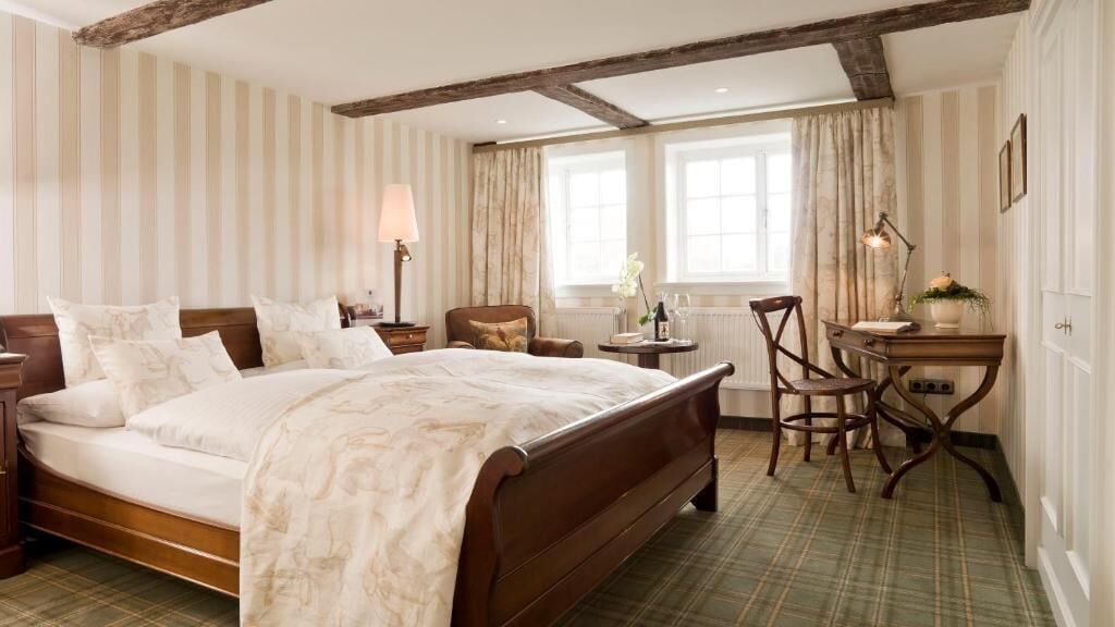 A hotel room with a large bed, a desk, a chair, and a window with curtains.