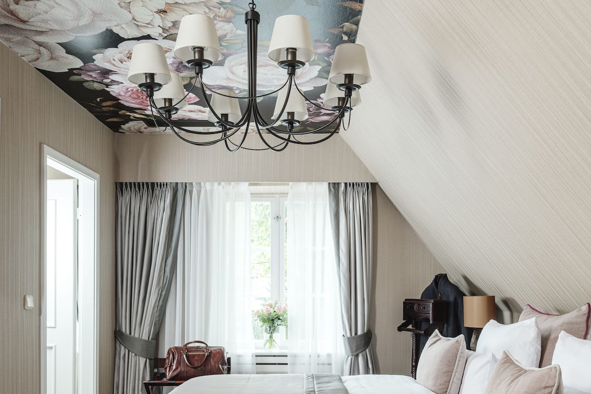 Een slaapkamer met een groot bed, een kroonluchter, uitzicht op de omgeving en een raam met gordijnen.