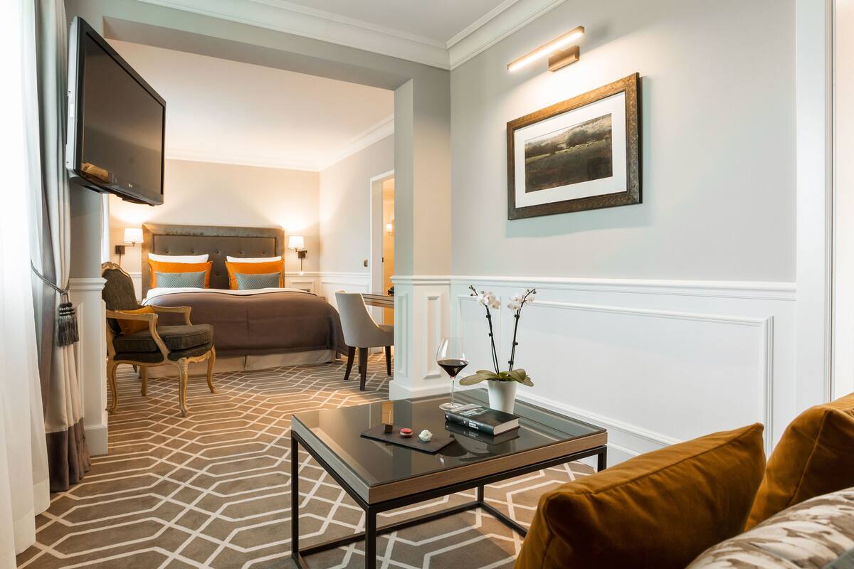 Een hotelkamer met een groot bed, een bureau, een stoel, een aan de muur bevestigde televisie en een lijst aan de muur.