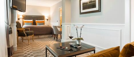 A hotel room with a large bed, a desk, a chair, a television mounted on the wall, and a framed picture on the wall.