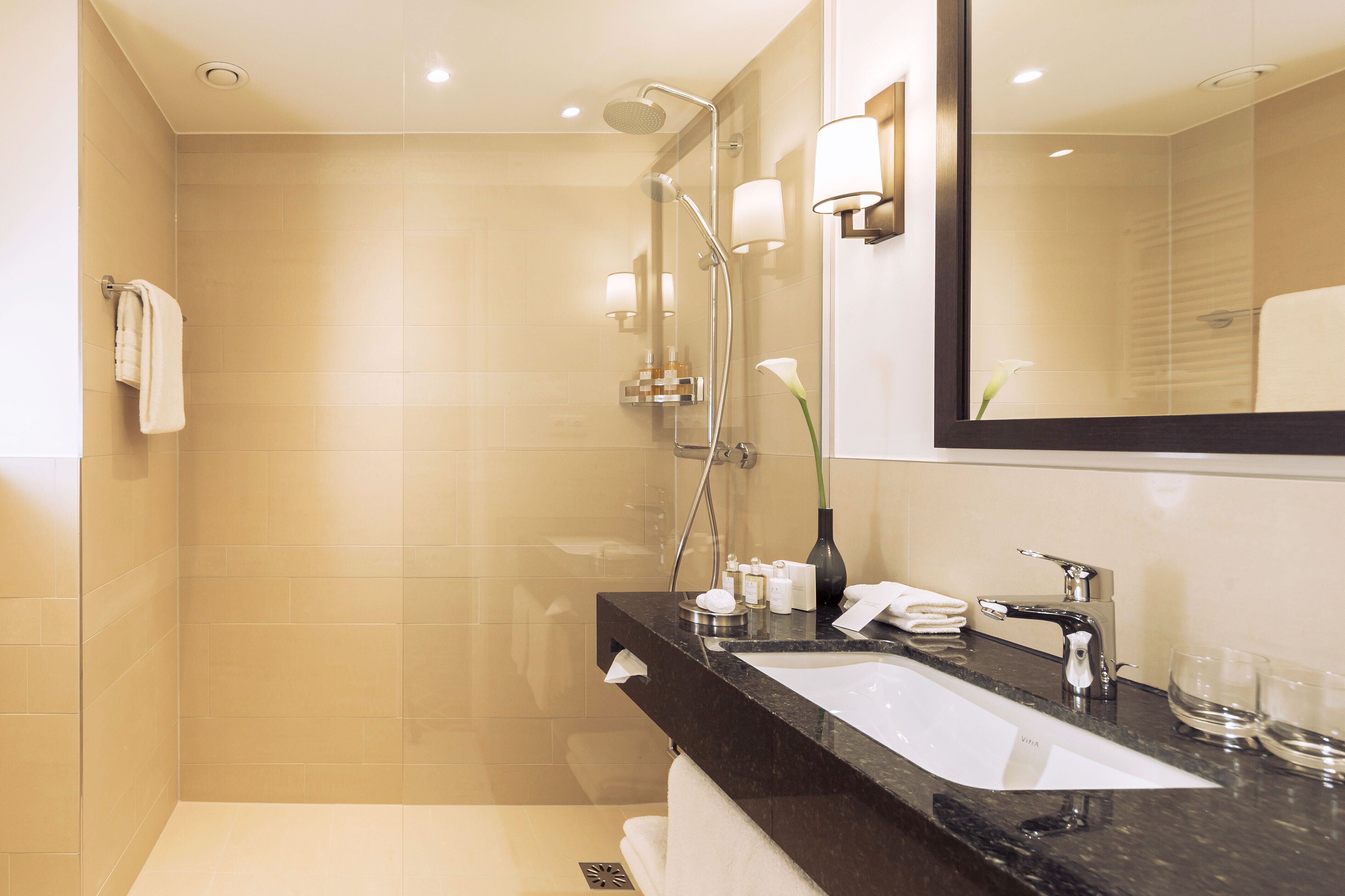 Un baño moderno con cabina de ducha de vidrio, lavabo de mármol negro y un espejo grande.