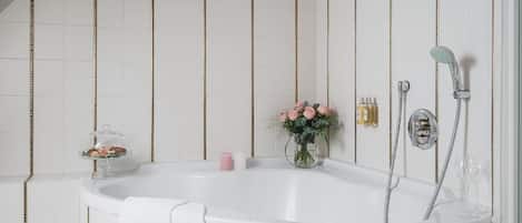 Un baño con una bañera independiente, cabina de ducha de vidrio y un florero con flores.