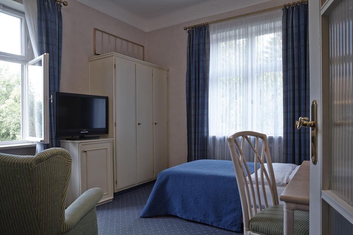 A hotel room with a bed, a television on a cabinet, a chair, and a desk.
