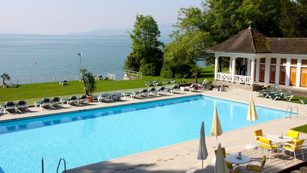 Una piscina con sillas de descanso y sombrillas, un pabellón y vistas al mar.