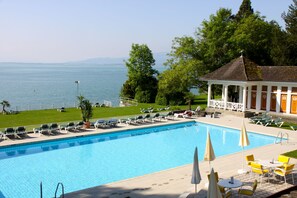 A swimming pool with lounge chairs and umbrellas, a gazebo, and a view of the sea. - Hotel Bad Schachen (Lindau)