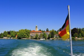 Une rivière avec un mât sur lequel flotte un drapeau, un bâtiment doté d’une tour et des arbres le long de la rive.