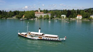 Un barco de paseo fluvial con varios niveles y una torre destacada, amarrado cerca de un muelle con edificios y árboles.
