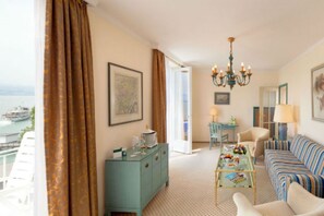 Un salon avec vue sur la mer, un canapé, une table basse, un buffet bleu et un lustre.