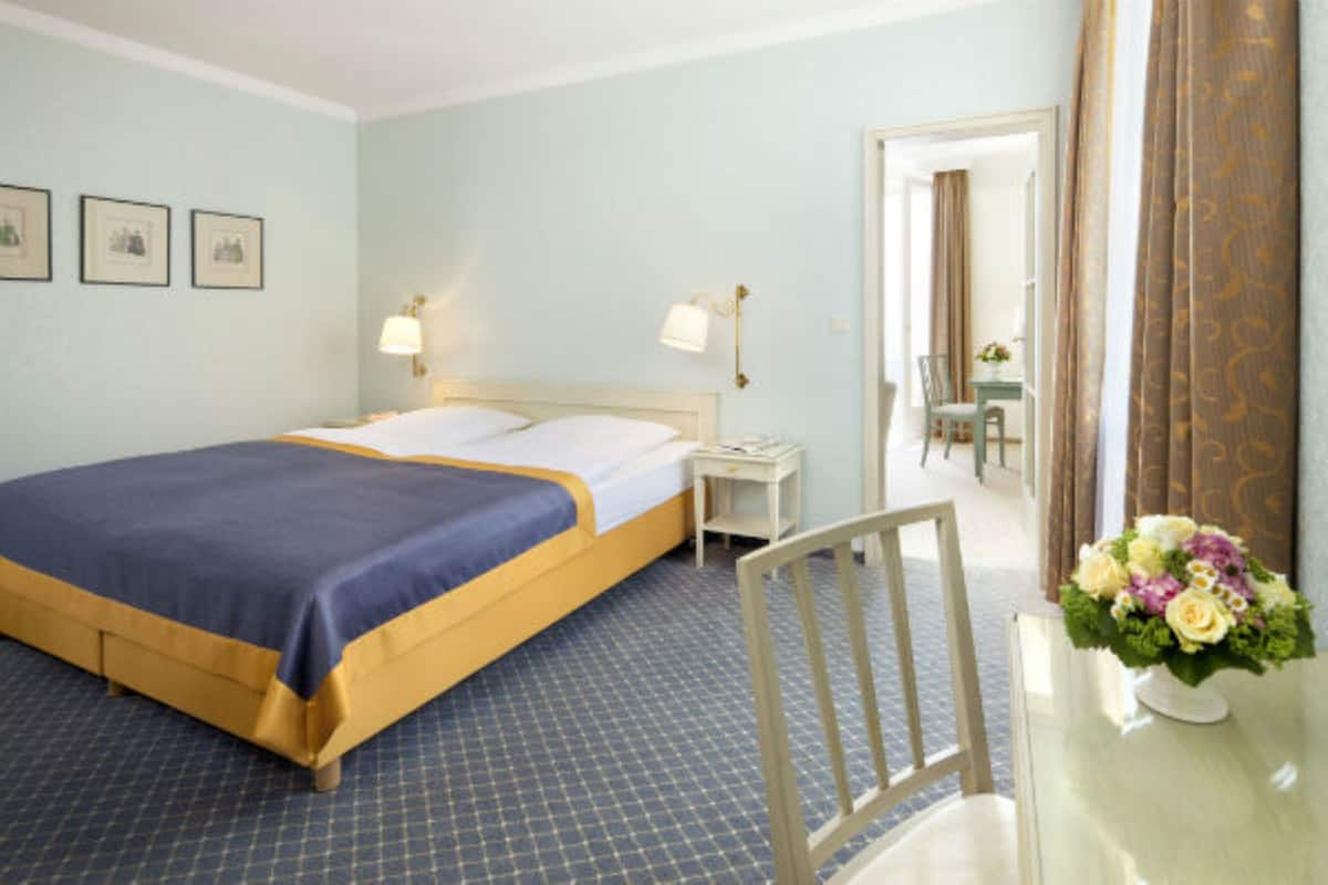 A hotel room with a bed, bedside tables, a chair, and a vase of flowers.