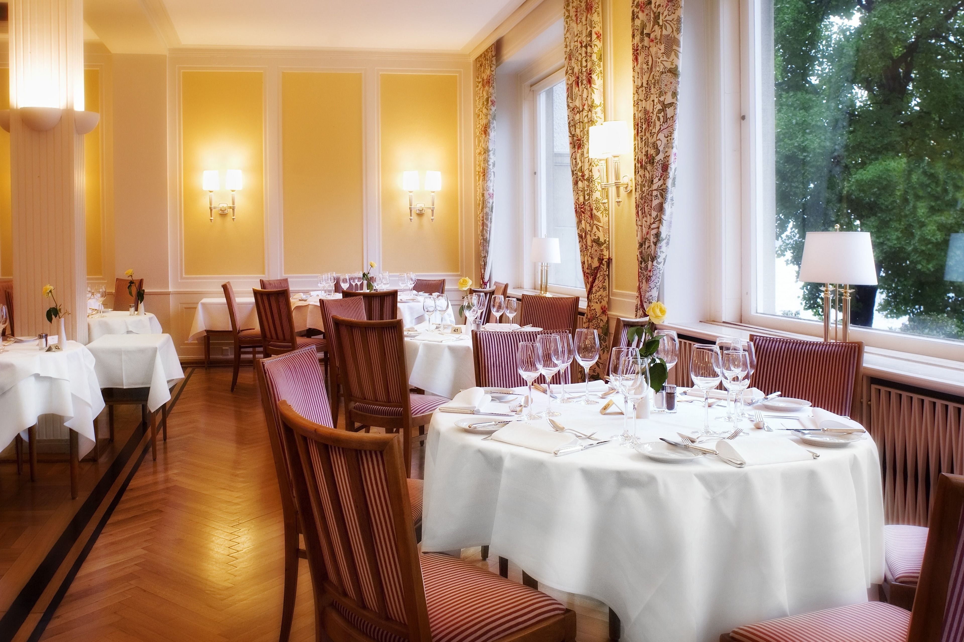 Un restaurante con mesas redondas dispuestas para comer, manteles blancos y sillas a rayas.