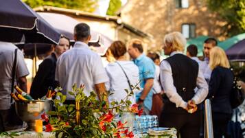 A group of people at an outdoor event with a table featuring a floral arrangement and a champagne bucket.