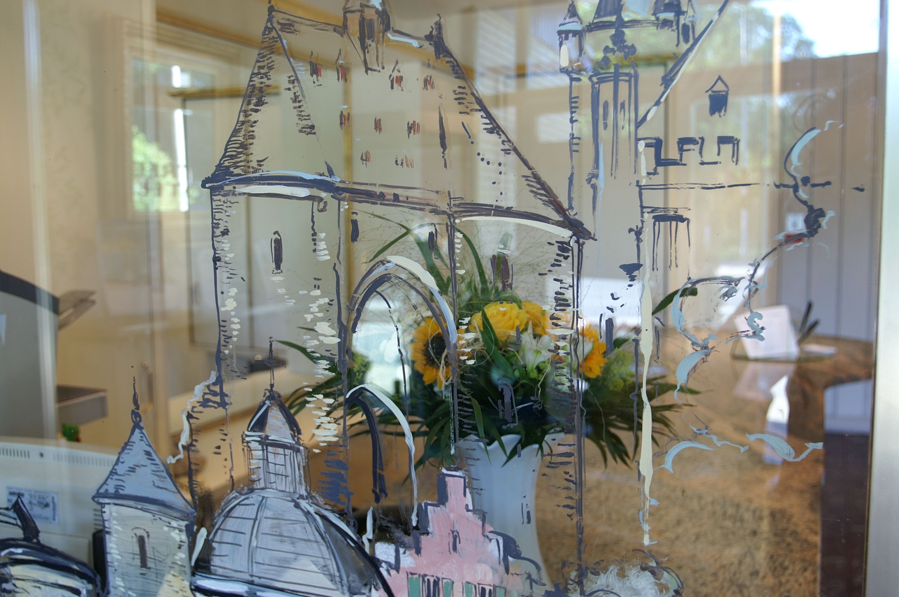 A stained glass window with architectural designs and a vase with yellow flowers.