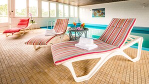 Ein Poolbereich mit zwei gestreiften Liegestühlen, einem Tisch mit Getränken und Blick auf den Pool.