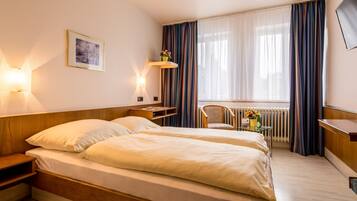Ein Hotelzimmer mit zwei Betten, einem Schreibtisch, einem Sessel, einem Heizkörper und einem Fernseher.