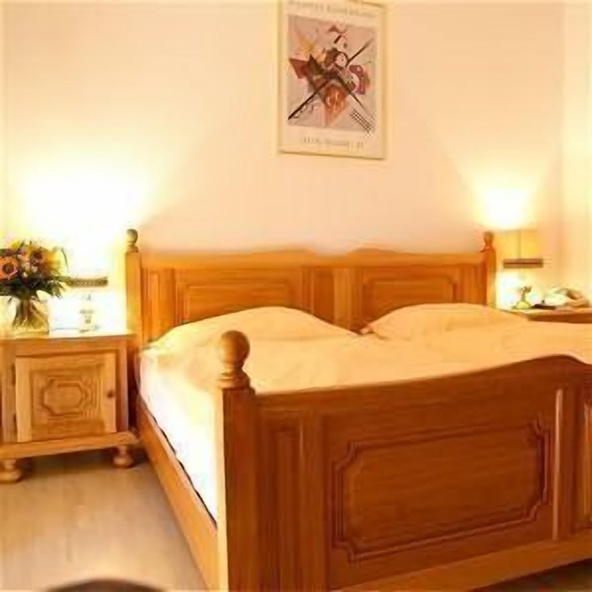 A wooden bed with a headboard, a bedside table with a lamp, and a framed picture on the wall.
