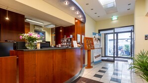 En hotellreception med en bardisk i trä, en vas med blommor, en digital skärm och en informationsskylt.