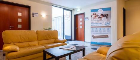 A hotel lobby with a yellow sofa, a coffee table, and a poster advertising breakfast.