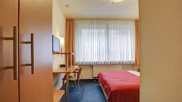 Et hotelværelse med seng, skrivebord, stol, fjernsyn og et vindue med gardiner.