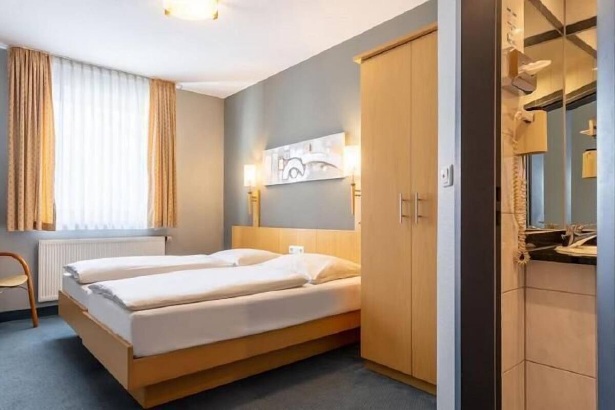 A hotel room with a bed, a chair, a TV, a wardrobe, and a window with curtains.