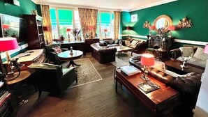 A cozy living room with a fireplace, comfortable seating, and a large window with curtains. - Hotel Ashley's Garden (Düsseldorf)
