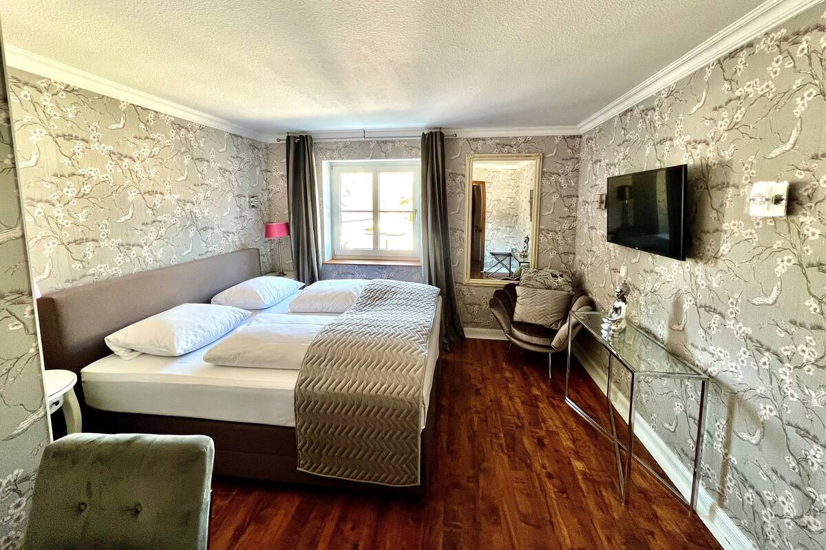 A bedroom with a large bed, a chair, a desk, and a TV.