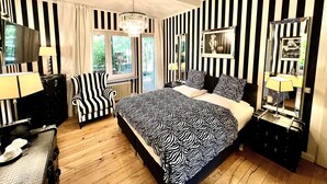 A hotel room with a zebra-striped bedspread, a black and white striped wall, a chandelier, a large mirror, and a view of the outdoors through the window. - Hotel Ashley's Garden (Düsseldorf)