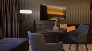 Une chambre d’hôtel moderne équipée d’un canapé, de deux fauteuils, d’une petite table et d’un téléviseur à écran plat fixé au mur.