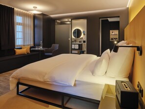 Une chambre d’hôtel dotée d’un grand lit, d’un coin salon avec une table et des chaises, d’un minibar et d’une salle de bain avec un miroir et un porte-serviettes.