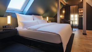 Une chambre d’hôtel moderne avec une lucarne, un grand lit, des lampes de chevet, une petite table et une chaise.