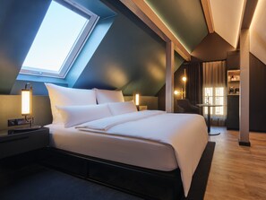 Ein modernes Hotelzimmer mit Dachfenster, einem großen Bett, Nachttischlampen, einem kleinen Tisch und einem Sessel.