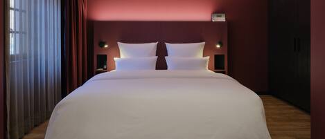 A large bed with white linens in a room with red walls and a wooden floor.