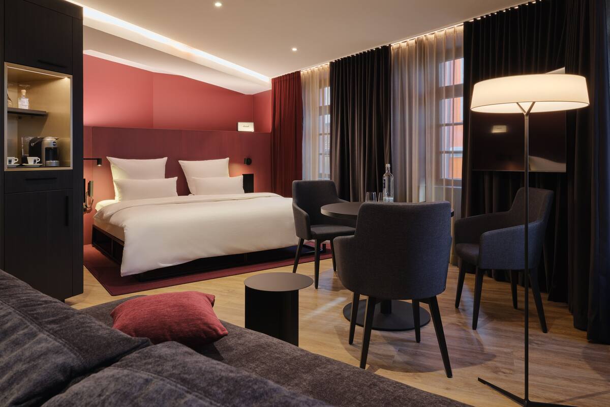 Une chambre d’hôtel moderne dotée d’un grand lit, d’un coin salon avec une table et des chaises, d’un canapé et d’un bureau avec une lampe.