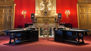Une pièce richement décorée, avec un grand lustre, des murs rouges et deux tables surmontées de vitrines.