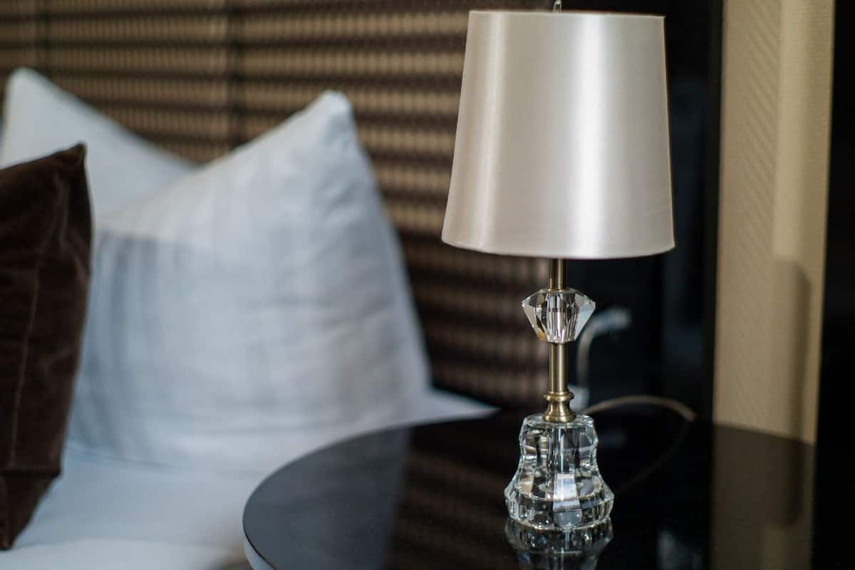 Ein Hotelzimmer mit einem Bett, einem runden Tisch mit einer Lampe und einem Fenster mit Jalousien.