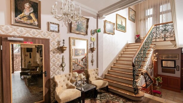 A grand lobby with a staircase, ornate wall decorations, and classic furniture. - City Hotel Kaiserhof (Offenbach am Main)