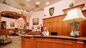 A reception area with a wooden counter, a receptionist, a chandelier, and framed artwork on the walls. - City Hotel Kaiserhof (Offenbach am Main)