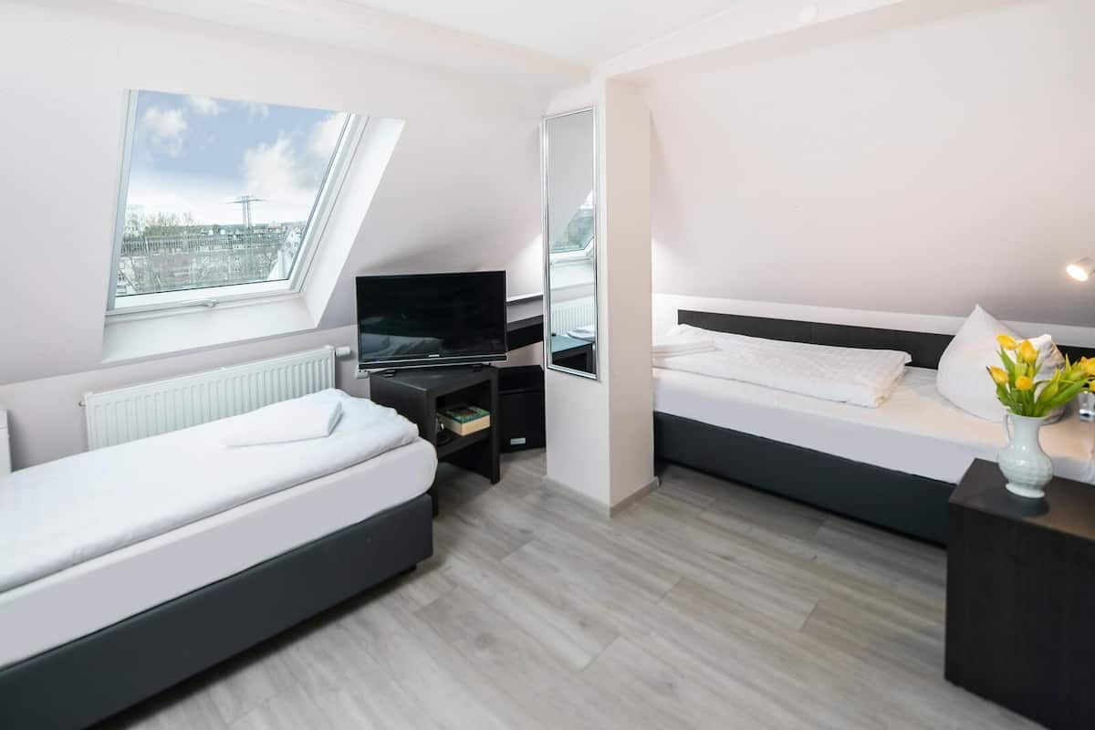Ein modernes Schlafzimmer mit zwei Betten, einem Fernseher und einem Fenster mit Blick auf die Stadt.