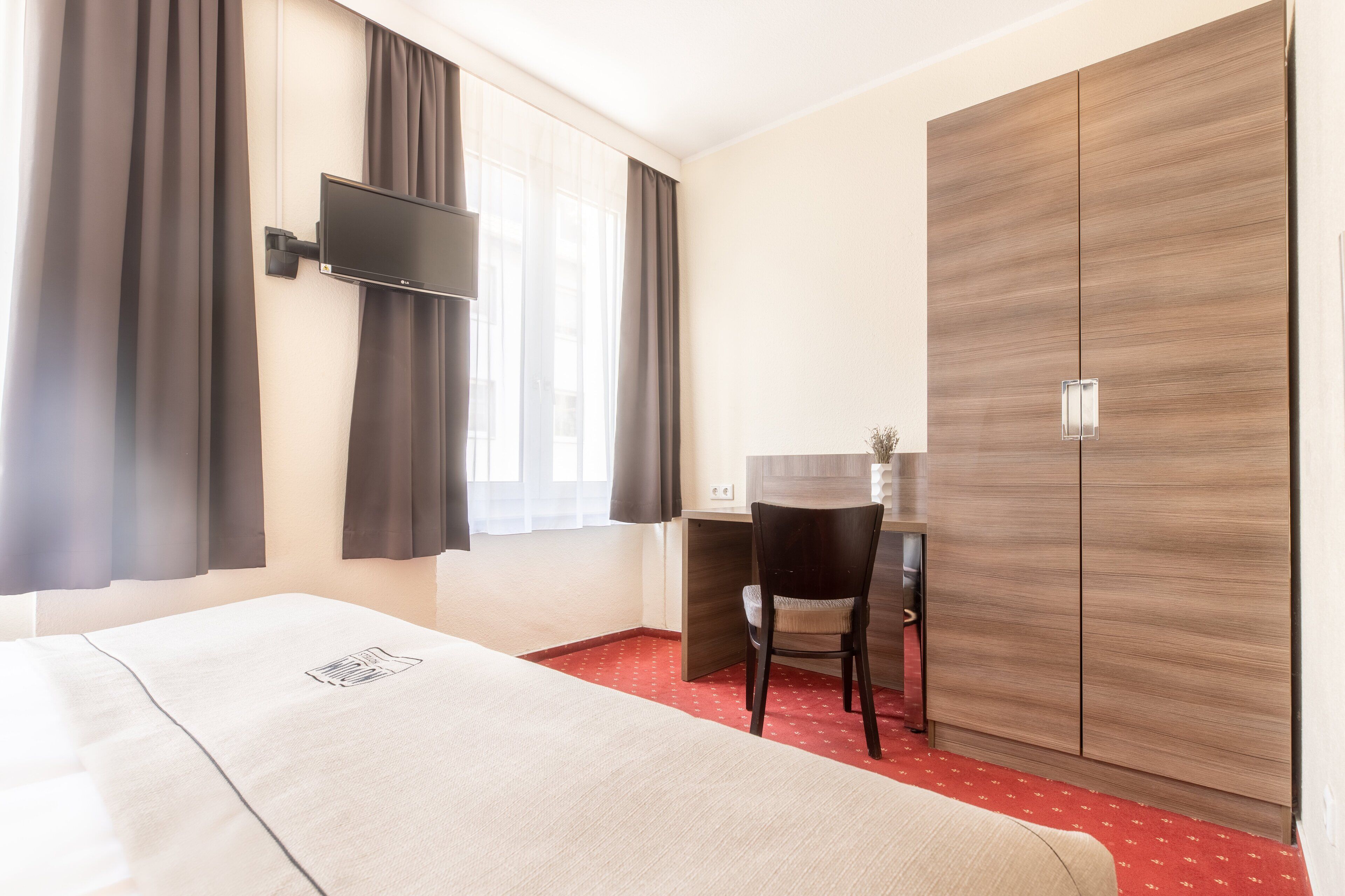Une chambre d’hôtel comprenant un lit, un bureau, une chaise, une télévision et une armoire.