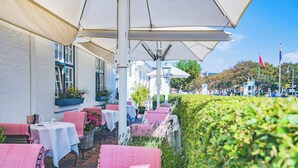 An outdoor café with tables and chairs, covered by umbrellas, and a hedge along the side. - Hotel Stadt Hamburg (Sylt)