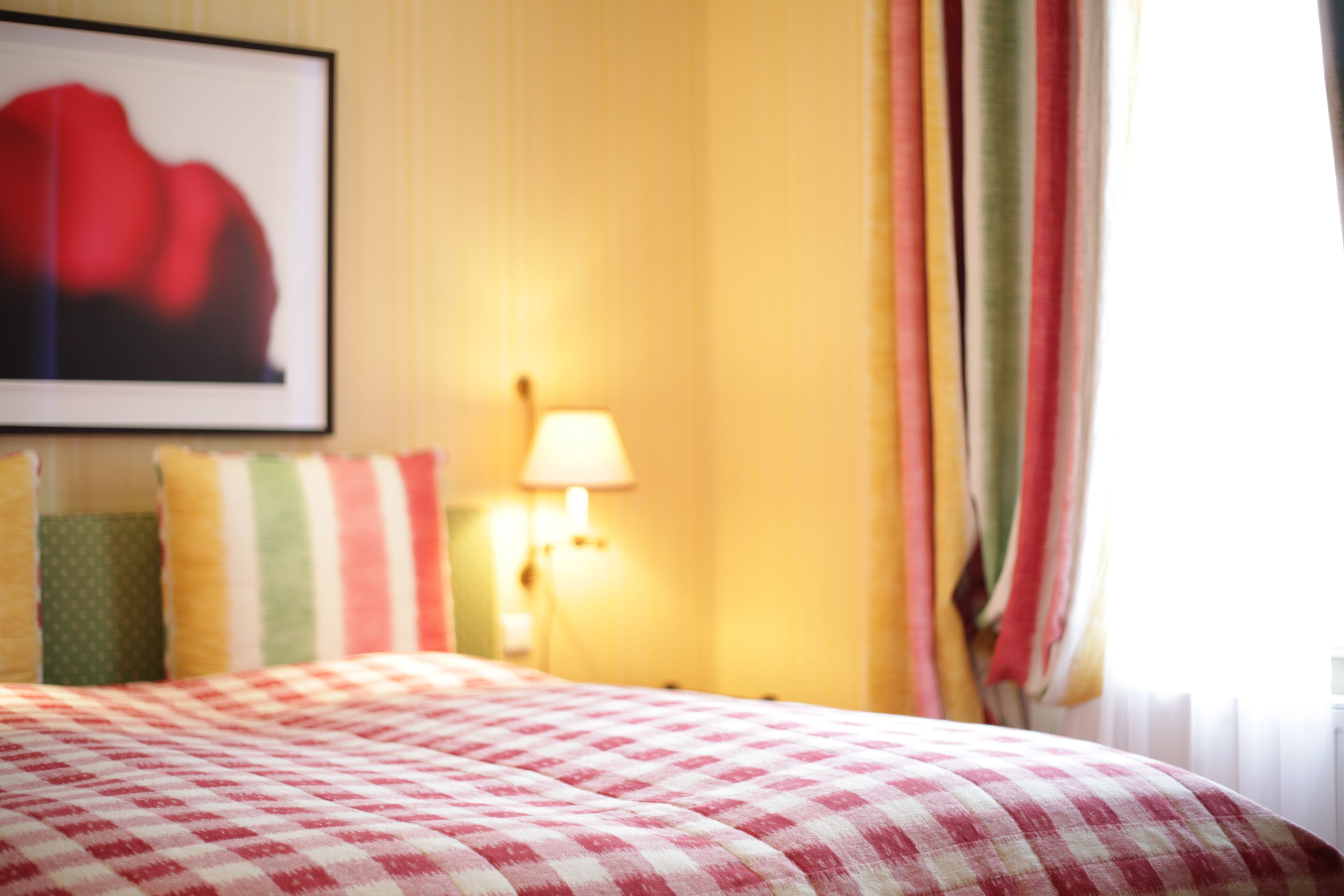 A bed with a checkered bedspread, a wall-mounted lamp, and a framed picture on the wall.